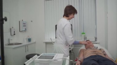 Elektrokardiyogram için tıbbi ekipman. Erkek hastaya EKG testi yapan doktorlar. Kalp krizi teşhisi, taşikardi. Elektrokardiyografi prosedürü. Kardiyolog kontrol testi yapıyor.. 