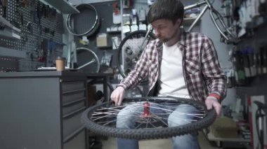 Yorgun bisiklet tamircisi bisiklet dükkanında tekerlek tamir eder, esner ve kahve içer. Yorgun adam bisiklet teknisyeni atölyede bisiklet tekerleğini tamir ediyor, gevezelik ediyor ve kahve içiyor. Yorgun bisiklet mühendisi. 