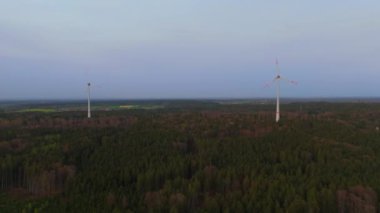 Ormanlı kırsal kesime kurulmuş rüzgar tarlası türbinlerinin hava görüntüsü. Doğanın enerjisini kullanarak güç üretiyor. Teknolojiyi doğanın ortamında birleştirmek. Bulutlu gökyüzü. Elektrik üretimi. 