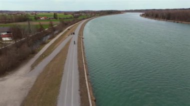 Bisikletçiler, Almanya 'nın Bavyera eyaletinde Rosenheim nehri boyunca bisiklet yolu üzerinde bisiklet sürerler. Ben Innradweg bei Rosenheim. Deutschland 'da geniş bir nehir boyunca çakıllı bisiklet yolu. Üst Bayern 'de döngü. 