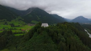 Schollanger burgkirche Fischen im Allgau, Bayern, Deutschland Luftaufnahme. Auwaldsee 'de. Dağa bakan nehir, dağlar ve Almanya 'nın Bavyera kentindeki Fischen' in tepesindeki güzel beyaz kilise.. 