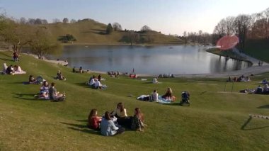 25 Mart 2022. Münih, Almanya. İnsanlar sıcak ve güneşli bahar havasında Münih 'teki Olimpik Park' ın yanındaki yeşil çimlerde dinleniyorlar. Olympiapark Münih. Olympiaberg ve Olympiasee in Olympiapark. 