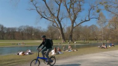 22 Mart 2022. Münih, Almanya. İnsanlar baharda güneşli ve sıcak havalarda Englischer Bahçesi 'ndeki Isar Nehri yakınlarındaki yeşil çimlerde dinleniyorlar. İnsanlar sıcak günün tadını çıkarıyorlar, Münih 'teki Isar Nehri yakınlarında güneşleniyorlar.. 