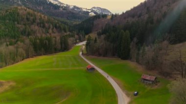 Bisikletçiler, Bavyera Alpleri 'ndeki dağ vadisinde asfalt yolda, baharda Almanya' da karla kaplı dağların manzarasıyla bisiklet sürerler. İnsansız hava aracı görüntüsü. Alp yolu boyunca seyahat eden hava manzaralı bisikletçi. 