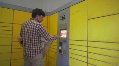 Sarı self servis posta terminali. Paket yollayan adam. Paket toplama noktası, bağlantısız self servis terminali, paket teslimatı. Kutuyu paket makinesine koyan adam. Paket depolama için depozito