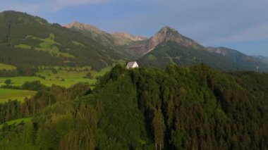 Schollanger burgkirche Fischen im Allgau, Bayern, Deutschland Luftaufnahme. Auwaldsee 'de. Dağa bakan nehir, dağlar ve Almanya 'nın Bavyera kentindeki Fischen' in tepesindeki güzel beyaz kilise.. 