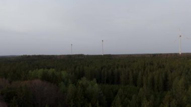 Ormanlı kırsal kesime kurulmuş rüzgar tarlası türbinlerinin hava görüntüsü. Doğanın enerjisini kullanarak güç üretiyor. Teknolojiyi doğanın ortamında birleştirmek. Bulutlu gökyüzü. Elektrik üretimi. 
