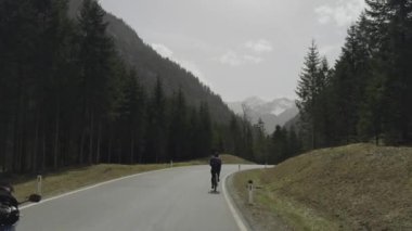 Erkek bisikletçi, güneşli bir baharda Avusturya dağlarında asfalt bir yolda bisiklet sürüyor. Alplerde yol bisikleti. Tyrol, Avusturya 'da arabaları ve motosikletçileri olan bir yolda bisiklet sürüyor. 