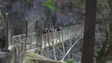 30 Mart 2024, Fussen, Almanya. Marienbrucke girişi ya da Kraliçe Marys Köprüsü yaya köprüsü uçurum üzerindeki Neuschwanstein Kalesi manzaralı. İnsanlar Neuschwanstein 'e yüksek köprüden bakıyor 