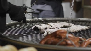 Şeflerin elleri kışın Almanya 'da Noel pazarında ateşte asılı duran metal ızgarada sosis pişiriyor. Akşamları Noel Fuarı 'nda farklı türde sosisli barbekü. Bayerische Wurste. 