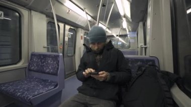 Hamburg 'da metroda seyahat eden mavi koltukta oturan ve kışlık kıyafetler giymiş akıllı telefon kullanan bir adam. Hamburg metro banliyösü işe gidip gelirken internette geziniyor. Hamburger U-Bahn. 
