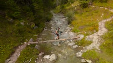 Bisikletçi, Almanya, Bavyera 'dan omzunda bisikletle derme çatma ahşap köprüden dağ nehrinden geçiyor. Bisikletçi ahşap hendeğin üzerinden dağlık kayalık nehri geçiyor.. 
