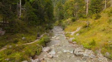 Bisikletçi, Almanya, Bavyera 'dan omzunda bisikletle derme çatma ahşap köprüden dağ nehrinden geçiyor. Bisikletçi ahşap hendeğin üzerinden dağlık kayalık nehri geçiyor.. 