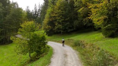 Eylül ayında Almanya 'nın Bavyera şehrinde çakıl bisikleti süren erkek bisikletçinin hava manzarası. Arkasından bisikletlinin drone görüntüsü dağlardaki Bavyera ormanında çakıllı bisiklet rotası boyunca gidiyor.. 