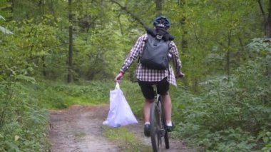 Ormanda bisiklet sürerken gidonu çöp torbasıyla gezmek, ormanda bisiklet gezisi sırasında çöp ve plastik temizlemek. Ekoloji teması, kirlilik, çöp ve plastik atılıyor.