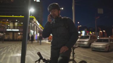 Kasklı ve sırtında sırt çantasıyla gezen bir bisikletçi. Şehirde akşam saatlerinde sokak lambaları ve el sallayarak tanıdık insanlara sesleniyor. Merhaba, buraya bakın, buradayım. Akşamları bisikletli bir yolcu.. 