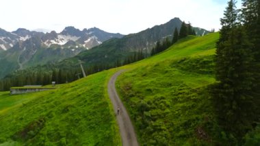 Yazın Alpler 'de kayak merkezinde bisiklet süren hava manzaralı bisikletçi. Bisikletçi Almanya 'nın Bavyera dağlarındaki dağ tatil beldesinde çakıllı bisikletle seyahat ediyor. Alp yamaçlarında bisiklet gezileri 