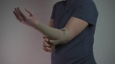 Tromboz koruyucuları. Kadın, gri arka planda sol kolundan sıkıştırma kolunu çıkarıyor. Etkili anti-tromboz tedavisi, damar sağlığı ve kan akışını iyileştirmek için sıkıştırma kolları içerir.. 
