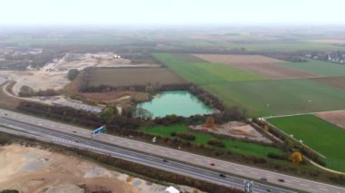 Almanya 'da aktif bir kum ocağının yanında açık mavi suyla dolu bir taş ocağının havadan görüntüsü. Sahne, insan sanayisiyle doğal güzelliğin çelişkili olarak yakınlardaki bir otoyol ve sanayi bölgesini içeriyor.
