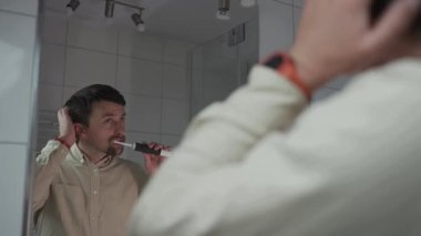 Aynadaki yansımalar, işten önce gömlekli bir adam dişlerini siyah ultrasonik elektrikli diş fırçasıyla fırçaladı, kendini beğendi, saçını beğendi ve aynada kendine bakarken onu düzeltti.. 