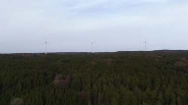 Ormanlı kırsal kesime kurulmuş rüzgar tarlası türbinlerinin hava görüntüsü. Doğanın enerjisini kullanarak güç üretiyor. Teknolojiyi doğanın ortamında birleştirmek. Bulutlu gökyüzü. Elektrik üretimi. 