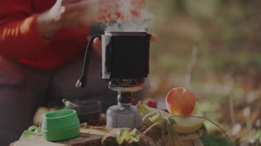 Erkek turist, sonbahar ormanlarında öğle yemeği arasında sandviçten hoşlanır. Ağaç kütüğünün yanında otururken, portatif kamp malzemeleri ve çatal bıçak kullanıyor, yemeğini hazırlarken ve yerken dışarıyı kucaklıyor.. 