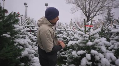 İnsanlar Noel 'den önce kışın karlı havada açık hava pazarından Noel ağacı seçerler. Erkek, Noel arifesinin hemen önünde, karlı havada, yerel sokak pazarından Noel ağacını seçiyor.. 