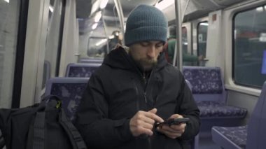 Hamburg 'da metroda seyahat eden mavi koltukta oturan ve kışlık kıyafetler giymiş akıllı telefon kullanan bir adam. Hamburg metro banliyösü işe gidip gelirken internette geziniyor. Hamburger U-Bahn. 