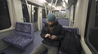 Hamburg 'da metroda seyahat eden mavi koltukta oturan ve kışlık kıyafetler giymiş akıllı telefon kullanan bir adam. Hamburg metro banliyösü işe gidip gelirken internette geziniyor. Hamburger U-Bahn. 