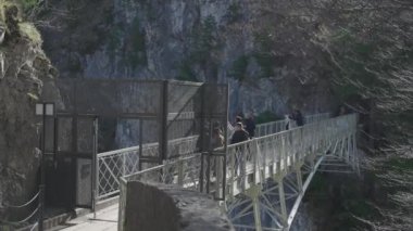 30 Mart 2024, Fussen, Almanya. Marienbrucke girişi ya da Kraliçe Marys Köprüsü yaya köprüsü uçurum üzerindeki Neuschwanstein Kalesi manzaralı. İnsanlar Neuschwanstein 'e yüksek köprüden bakıyor 