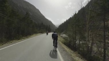 Erkek bisikletçi, güneşli bir baharda Avusturya dağlarında asfalt bir yolda bisiklet sürüyor. Alplerde yol bisikleti. Tyrol, Avusturya 'da arabaları ve motosikletçileri olan bir yolda bisiklet sürüyor. 
