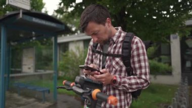 Adam şehirde elektrikli scooter kiralamak için akıllı telefon kullanıyor. Genç adam e-scooter 'ın parasını cep telefonuyla internet üzerinden ödüyor. Elektrikli araç kiralama teması. Kentsel çevre dostu ulaşım. 