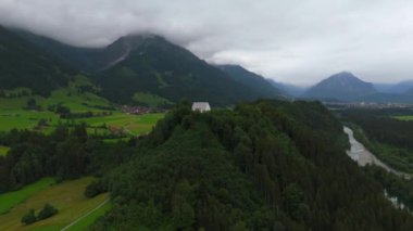 Schollanger burgkirche Fischen im Allgau, Bayern, Deutschland Luftaufnahme. Auwaldsee 'de. Dağa bakan nehir, dağlar ve Almanya 'nın Bavyera kentindeki Fischen' in tepesindeki güzel beyaz kilise.. 