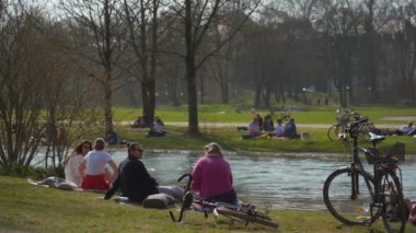 22 Mart 2022. Münih, Almanya. İnsanlar baharda güneşli ve sıcak havalarda Englischer Bahçesi 'ndeki Isar Nehri yakınlarındaki yeşil çimlerde dinleniyorlar. İnsanlar sıcak günün tadını çıkarıyorlar, Münih 'teki Isar Nehri yakınlarında güneşleniyorlar.. 