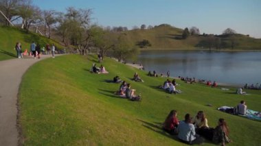 25 Mart 2022. Münih, Almanya. İnsanlar sıcak ve güneşli bahar havasında Münih 'teki Olimpik Park' ın yanındaki yeşil çimlerde dinleniyorlar. Olympiapark Münih. Olympiaberg ve Olympiasee in Olympiapark. 