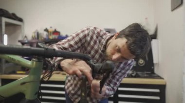 Bisiklet tamircisi bisiklet tamir atölyesindeki çalışma yerinde bisiklet gidonu etrafına bisiklet bandı sarar. Bisiklet mühendisi gidon bandı atölyedeki iş yerinde çakıl bisikleti üzerinde. 