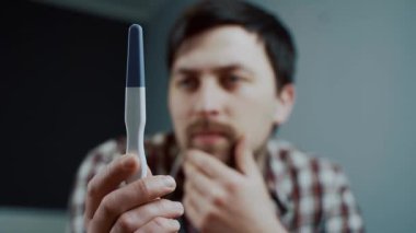 Düşünceli bir adam karısı tarafından yapılan hamilelik testine bakar. Stres altında başını tutar. Yüzündeki ifade hayal kırıklığını ve endişeleri gösteriyor. Beklenmedik hamilelik konusunda mutsuzluğunu ve isteksizliğini gösteriyor.