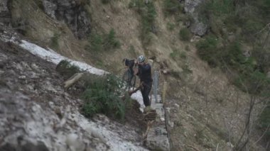 Bisikletçi dağlarda çığ üzerinden bisiklet çekiyor. Bisikletçi engelin içinde sıkıştı ve bisikletini elinde bisikletle bir buz kaydırağının içinden geçiriyor. Alplerdeki bisiklet rotasında çığ. 