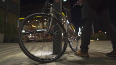 Korumalı maske takan erkek bisikletçi, bisiklet parkının dışındaki direğe şehir ışıklarının ışığında parlıyor. Bisiklet altyapısı eksikliği. Bisikleti şişir. 