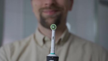 Elinde parlak, siyah bir elektrikli diş fırçası tutan ve açıp kapayan bir adam. Modern ağız temizliği, ultrasonik temizlik teknolojisi ve sağlıklı dişler için gelişmiş diş bakımı.. 