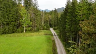 Eylül ayında Almanya 'nın Bavyera şehrinde çakıl bisikleti süren erkek bisikletçinin hava manzarası. Arkasından bisikletlinin drone görüntüsü dağlardaki Bavyera ormanında çakıllı bisiklet rotası boyunca gidiyor.. 