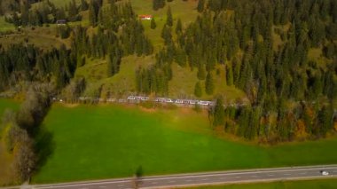 Almanya 'nın Bavyera kırsalında canlı bir sonbahar yeşilliği ile çevrili pikoresk Bayrischzell istasyonuna yaklaşan bölgesel trenin hava manzarası. Bahnhof 'daki Luftaufnahme Bölgesi' nden.. 