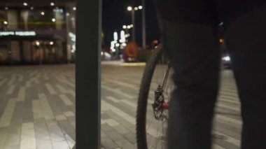 Korumalı maske takan erkek bisikletçi, bisiklet parkının dışındaki direğe şehir ışıklarının ışığında parlıyor. Bisiklet altyapısı eksikliği. Bisikleti şişir. 