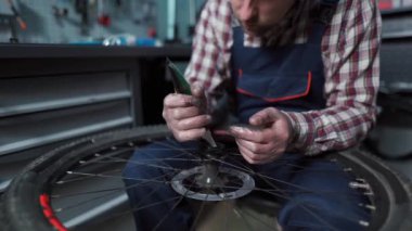 Bir atölyede profesyonel bir tamirci dağ bisikletini tamir ediyor, merkeze ve yönlere odaklanıyor. İş kıyafetleri giyer, düzgün performans sağlamak için uzman hizmeti, yağlama ve bakım sağlar.. 