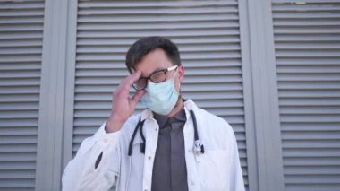 Beyaz önlüklü genç erkek doktor maskesini ve gözlüklerini çıkarıyor. Öfke, hayal kırıklığı ve yorgunluk gösteriyor. Kliniğin dışında dururken zor bir vakayı, işyeri stresini ya da kaybettiği bir hastayı düşünüyor.