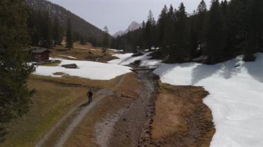 Avusturya ya da Almanya 'da dağ bisikleti üzerinde bisiklet süren insanların hava manzarası. İnsansız hava aracı eriyen karı, nehirleri, dereleri, bir yaya köprüsünü ve baharda dağın tepesindeki bir platonun yakınındaki bir kulübeyi yakalar.. 