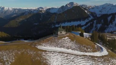 Kapelle Heilig Kreuz Rottach-Egern Tegernsee. Wallbergkapelle, Tegernsee Gölü 'ne tepeden bakan Wallberg Dağı ve güneşli bahar havasında gün batımında karla kaplı dağ sıraları. Alplerin zirvesindeki şapel. 