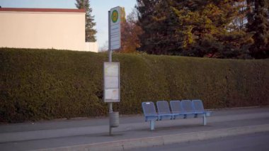 Sonbahar sezonunda Bavyera, Almanya 'da otobüs durağı. Sergide mavi banklar, yeşil bir çit, bir zaman çizelgesi ve çatısı ve insanları olmayan sonbahar ağaçları yer alıyor.. 