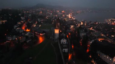 Musegg Wall ve dokuz kulesi geceleri İsviçre 'nin Lucerne kentindeki parlayan şehre bakıyor. Lucerne 'in ortaçağ savunması. Museggmauer Luzern und ihre neun Tuerme Luftaufnahme bei Nacht. 