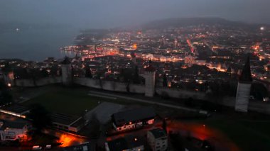 Musegg Wall ve dokuz kulesi geceleri İsviçre 'nin Lucerne kentindeki parlayan şehre bakıyor. Lucerne 'in ortaçağ savunması. Museggmauer Luzern und ihre neun Tuerme Luftaufnahme bei Nacht. 